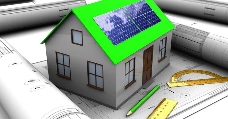 Ein Modell eines Hauses mit grünem Dach und Photovoltaikanlage steht auf einem Bauplan, rundherum liegen weitere Rollen Baupläne, Stifte und Lineale | Energieeffizient bauen