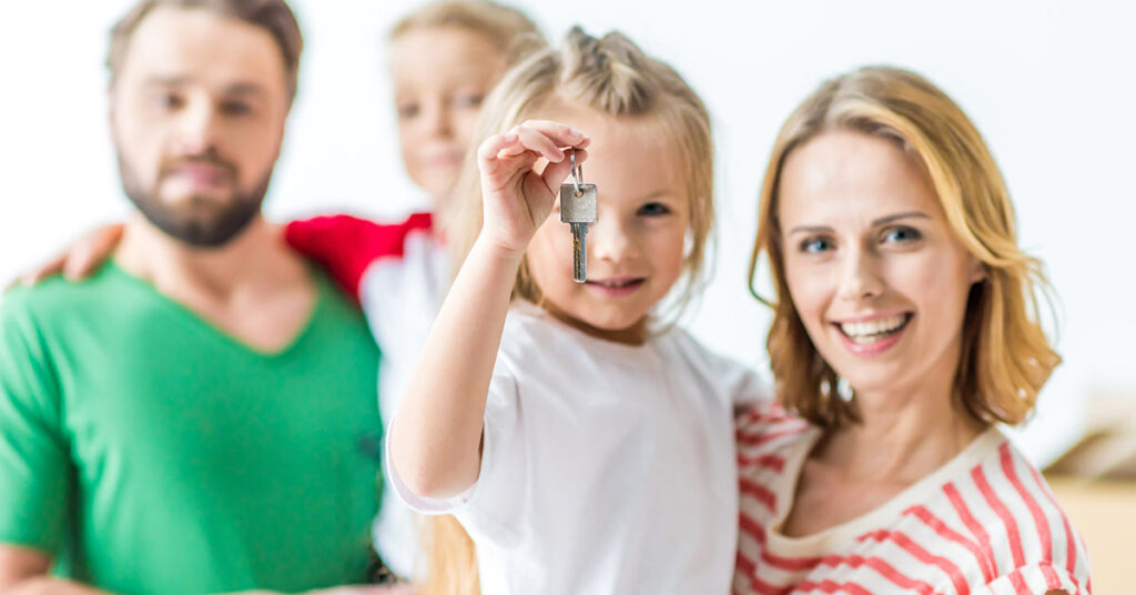 Eine Familie vor einem weißen Hintergrund lächelt, ein Mädchen hält einen Schlüssel in der Hand - Immobilienkauf