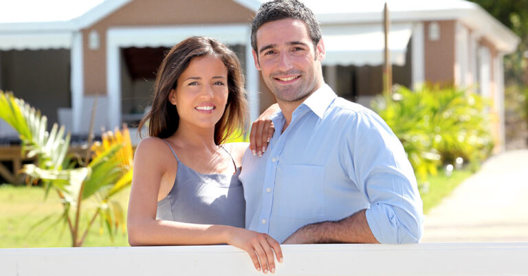 Ein lächelndes Paar steht vor einem Haus - Eigenheimbesitzer