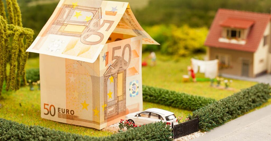 Modellhaus aus 50 Euro Scheinen in einem Garten mit einem weißen Spielzeugauto vor der Tür | Immobilienfinanzierung