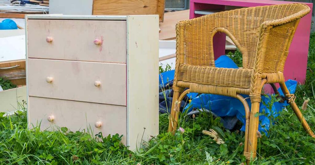 Alte Möbel, eine Kommode, ein Stuhl und anderes, stehen auf der Wiese vor dem Haus | Geerbte Immobilie entrümpeln