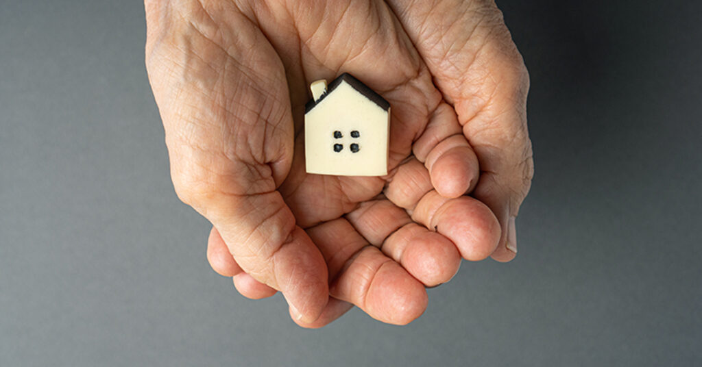 Inheritance concept. Elderly woman hands holds a little toy house. Inherited property idea; Erbschaftssteuer