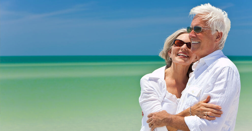 Ein älteres Paar mit Sonnenbrille vor einem blauen Himmer und Meer - Wohnen im Alter