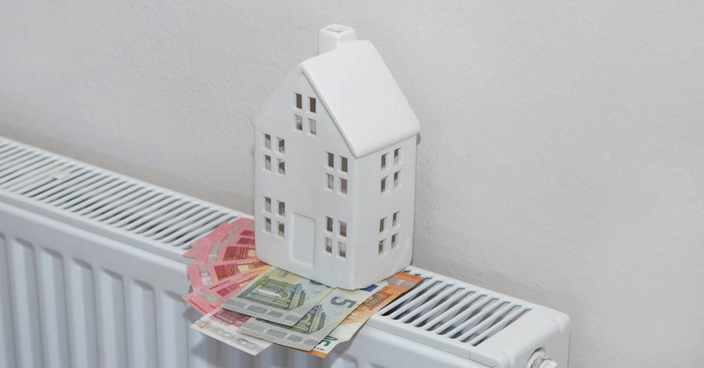 Ein weißes Minihaus auf einer Heizung mit Geldscheinen - Betriebskosten
