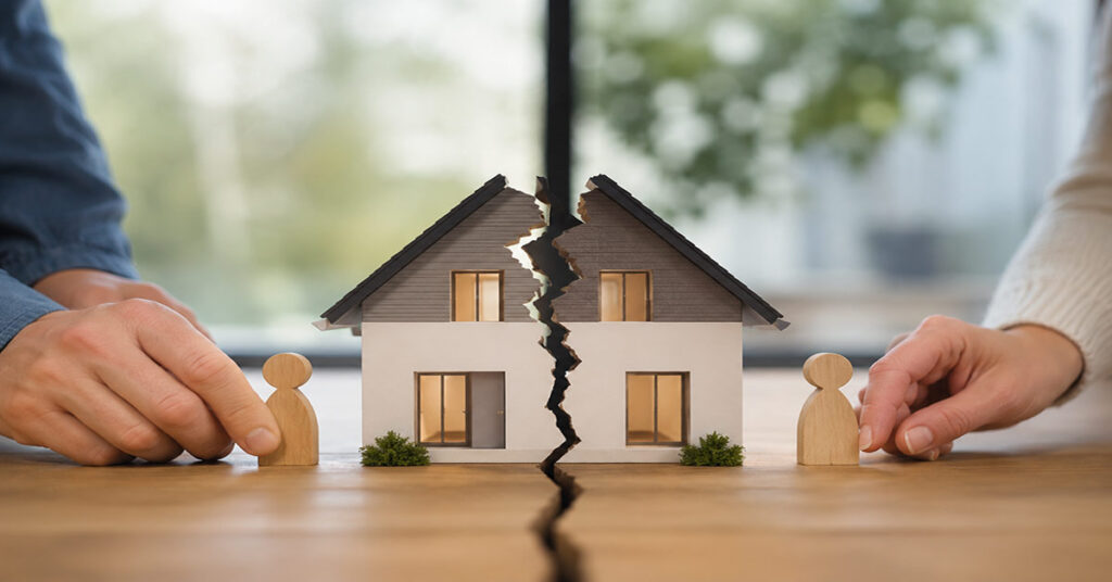 Geteiltes Hausmodell mit zwei Holzfiguren symbolisiert die Aufteilung einer Immobilie bei Trennung ohne Trauschein. I Trennung ohne Trauschein